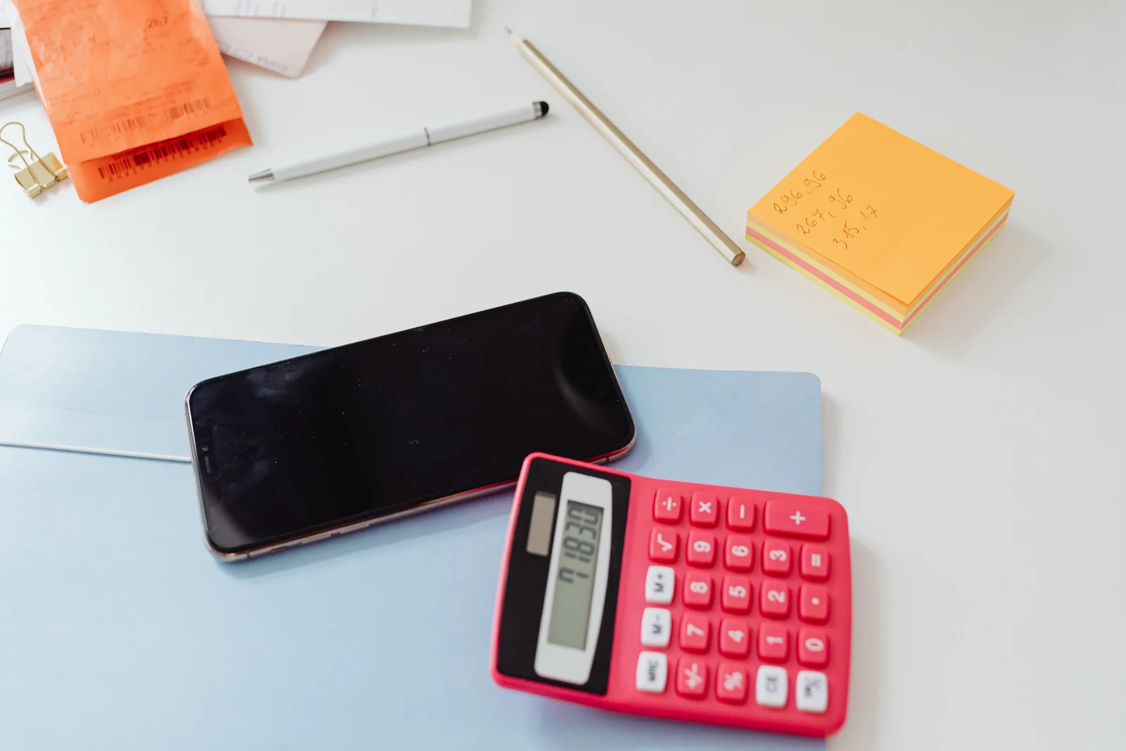 An organized office desk featuring a calculator, smartphone, and sticky notes on a white surface.