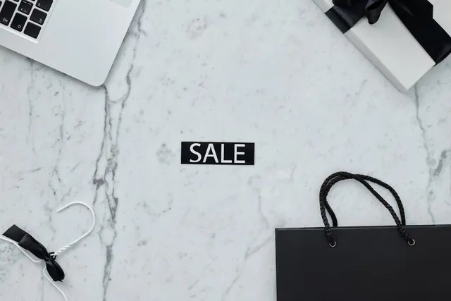 Minimalist sale-themed flat lay with laptop, gift, and shopping bag on marble. How eBay and Amazon order sync differs for UK multichannel sellers