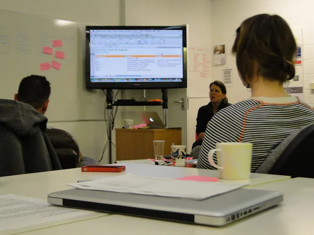 Students in front of large screen. In the foreground a closed laptop. Most likely qualitative data analysis in a spreadsheet, but it could also be any other kind of debriefing. When to trust a shopping feeds launch review and its sources