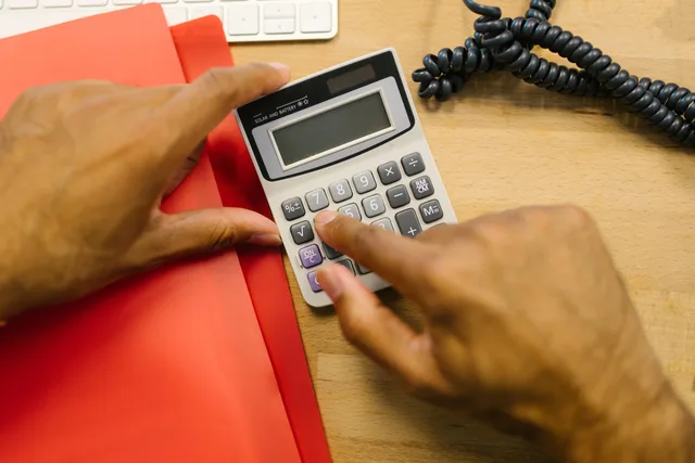 Close-up of hands using a calculator at a desk in an office setting. WooCommerce feed plugins: UK VAT, GBP and EORI fields